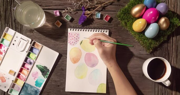 Happy Easter time-lapse – Asian woman hand painting a card of colorful Easter eggs with watercolor on wooden tabletop, morning time. Easter Holidays preparation at home. Handcraft and art concept.