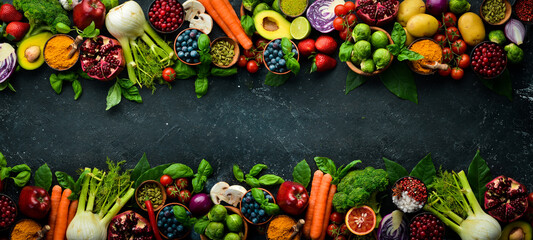 Fresh vegetables and fruits: fennel, avocado, pomegranate, berries, cabbage and basil. Organic healthy vegan food. On a black stone background.