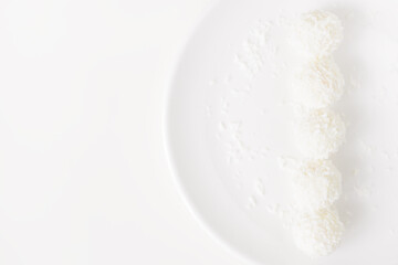 Food photography of natural vegetarian raw food candies with coconut. Close-up white round coconut candy on a white, delicate and airy background. Empty space for text. Flat lay top-down.