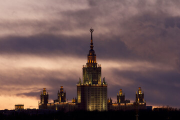 Silhouette of Moscow State University against the background of a purple sunset with clouds.