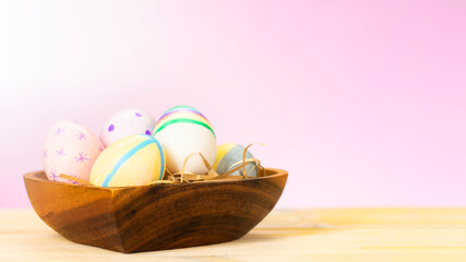 Fototapeta premium Colorful easter eggs on a wooden plate on a table on a pink background