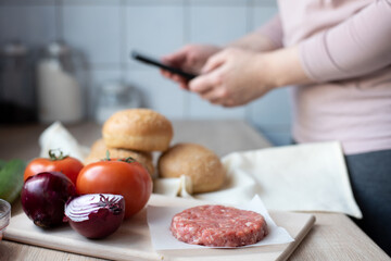 Cooking hamburger at home, a woman looking for the recipe in the phone in the kitchen with groceries.