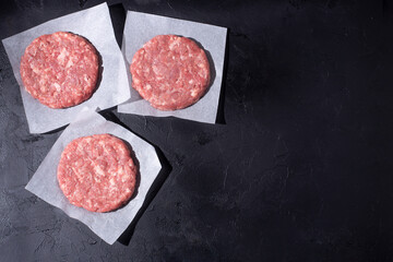 Three raw beef patties for burger on the black background.