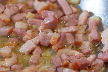 Onion pieces and bacon cubes frying