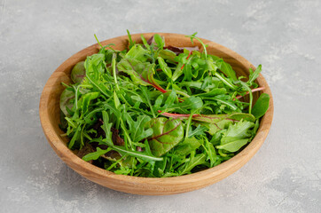 Mix of fresh salad leaves in a wooden bowl on a gray concrete background. Healthy food. Copy space.