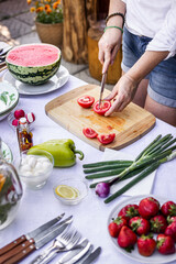 Preparing mediterranean dish for garden party. Woman is chopping red tomato on cutting board for vegetable salad