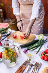 Obraz na płótnie Canvas Preparing vegetable salad outdoors. Woman chopping red tomato on cutting board