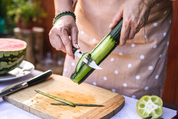 Woman peeling cucumber. Making fresh vegetable salad outdoors