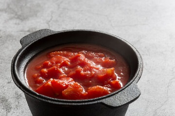 Chopped tomatoes cooked in a cast iron pot.  On a concrete background