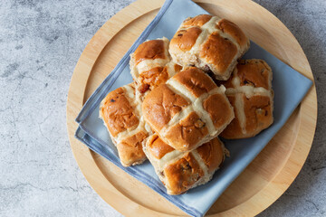 Hot cross buns stacked on a round wooden serving board and cloth.  Easter food concept