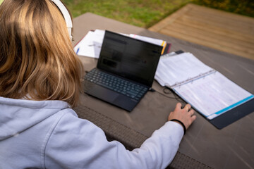 Une étudiante de dos travaille sur sa terrasse avec un ordinateur et un casque sur les oreilles - 420133870