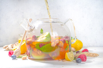 

Fruit and berry tea in teapot. Hot drink with lemon, mint, blueberry, ginger, orange, apple. Hot flavored steam beverage copy space

