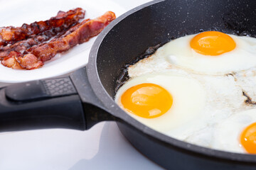 Fried eggs and bacon cooking in a skillet or pan. Idea for morning breakfast. Yellow yolks of eggs and red fried slices of bacon.