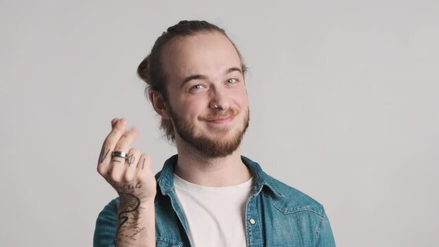 Young bearded man looking happy making money gesture rubbing fingers on camera over white background. Hands sign concept