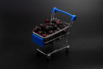 frozen black currant berries in a blue mini shopping cart on a black background