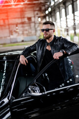 Fototapeta na wymiar Man in black jacket standing near opened car door. Fashionable portrairt of car and driver.
