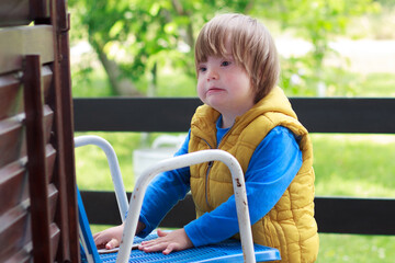 Portrait of cute adorable blondy toddler disabled boy with down sydrome while standing and holding...