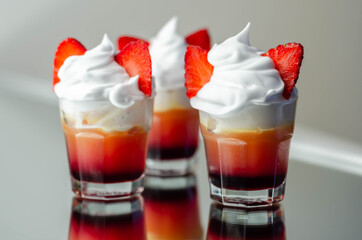 Colorful layered shots of drinks based on vodka, grenadine and orange juice decorated with whipped cream and pieces of strawberry in the shape of bunny ears