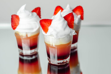 Colorful layered shots of drinks based on vodka, grenadine and orange juice decorated with whipped cream and pieces of strawberry in the shape of bunny ears