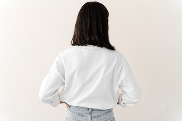 Millennial female wearing white t-shirt standing turning back to camera. Young woman standing isolated on white background in studio. Copyspace, corporate branding concept.