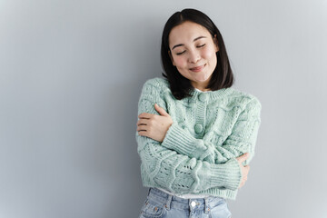 The dreamy girl, closing her eyes, will enjoy the memories. Girl in a knitted sweater on a gray...