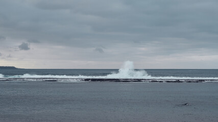 Fototapeta na wymiar Big tall waves at the beach hit breakwater. Winter season, windy and stormy weather. 