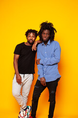 Obraz premium two african american guys posing cheerful together on yellow background, lifestyle people concept