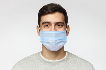 Young handsome man wearing sweatshirt and medical mask, standing isolated on gray background