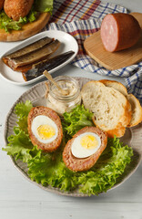 Scottish-style eggs cut in half on a plate with lettuce leaves, baguette slices and sauce. On a light wooden background, vertically