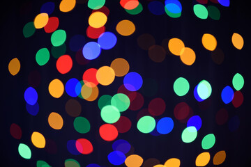 Christmas or New Year dark background. Festive glowing background. Defocused background with colorful blinking garland. Blurred bokeh.