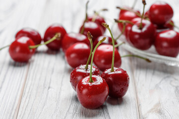 Fresh cherry berries with drops of water in a glass plate on a white wooden table. Close-up macro shot