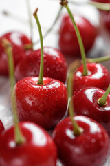 Fresh cherry berries with drops of water on a white wooden table. Close-up macro shot. Selective focus.