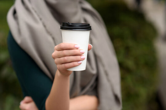 Young woman holds a paper cup with coffee or tea in her hands. Hot drinks to go. Close-up shot.