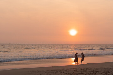 Kobiety spacerujące brzegiem oceanu o zachodzie słońca, ciemno pomarańczowy nastrojowy...