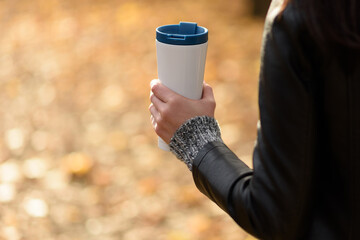 Woman in a leather jacket outdoors hold a eco friendly reusable coffee tumbler. Take coffee with a...