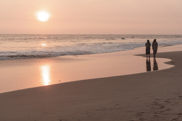 Fototapeta na wymiar Kobiety spacerujące brzegiem oceanu o zachodzie słońca, ciemno pomarańczowy nastrojowy krajobraz.