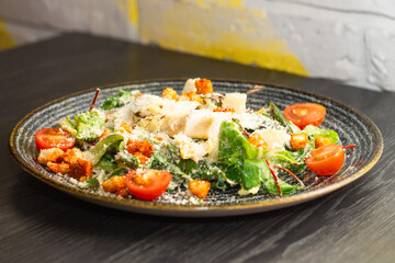 Caesar salad in dark clay plate on black wooden table