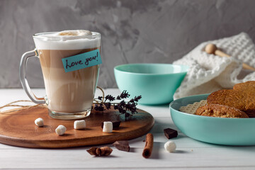 Coffee latte cup with Love you sticker on wooden tray with turquoise bowls with cookies on gray wall background
