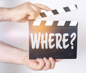 Obraz premium On a white background, a man holds a clapperboard in his hands on which it is written - WHERE