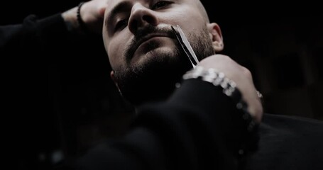 Close-up of barber cuts the hair by scissors at barbershop. Hairdresser's hands at working process. Barber making haircut of attractive bearded man in barbershop. Hairdresser at work. Beauty saloon.
