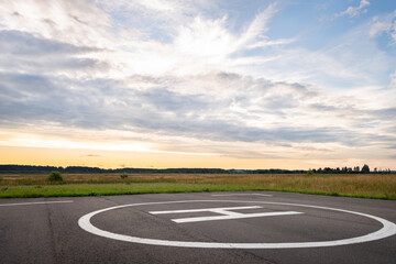 View of the private helipad on a warm summer evening. An asphalt helipad against the backdrop of a green field and a cloudy evening sky.