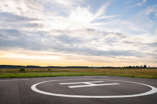 View of the private helipad on a warm summer evening. An asphalt helipad against the backdrop of a green field and a cloudy evening sky.