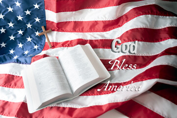 Open Holy bible and Wooden cross over American flag background. God bless America.