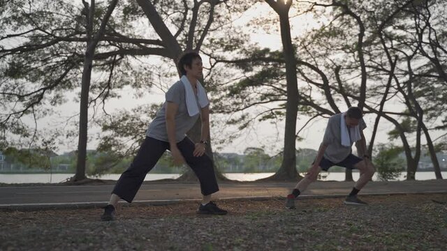 happy active senior couple exercise and stretching at park in evening sunset. smiley active asian elderly lover outdoor activity sharing good moment together. fitness duo mature workout at park.