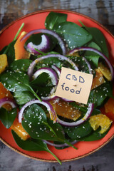 Selective focus. A note with the inscription CBD food in a plate of salad. Cannabis oil salad. Healthy salad with spinach and orange.