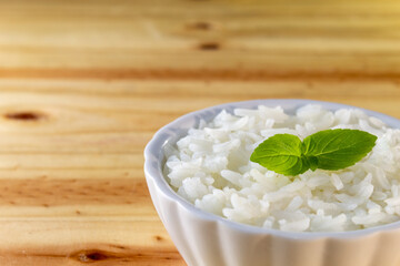 UMA BACIA COM ARROZ BRANCO E FOLHAS DE MANJERICÃO, SOBRE A SUPERFÍCIE DE MADEIRA.
