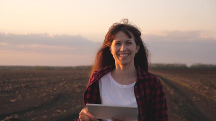 Business woman with modern gadget works online outdoors. Freelancer woman working in field. Farmer woman with tablet in field in rays of sunset. A woman agronomist checks the quality of sowing grain.