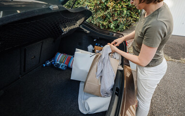 Overhead view of Young woman unloading car trunk with multiple bags after shopping near her garage door
