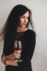 Beautiful young brunette woman in a black dress with a glass of red wine. Portrait of a woman in the room
