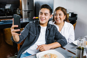 hispanic mother and her daughter smiling and posing for a photo while sitting by dinner at home in...